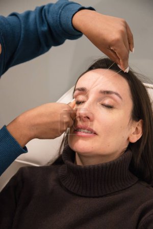 Caucasian woman removing hair from eyebrows with thread technique done by eyebrow stylist. Threading. Process Steps. Close up