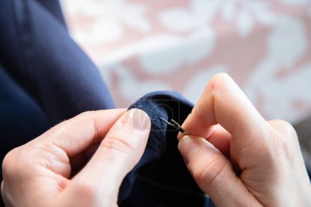 Detail of the hands of a caucasian woman doing sewing work in her home. Process and execution. Measuring, cutting and sewing to re-hem a pair of trousers.
