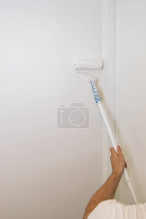 Foto de Trabajador pintando una pared. Renovación de la pintura en la pared. Imagen vertical y espacio de copia. - Imagen libre de derechos