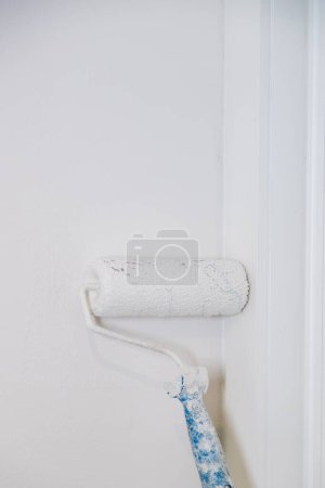 Foto de Trabajador pintando una pared usando rodillo y pintura blanca, renovación, remodelación de espacios. Imagen vertical. Cerrar y copiar espacio. - Imagen libre de derechos