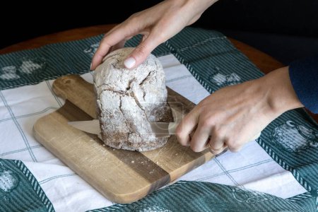 Broa de Avintes, traditional bread from Vila de Avintes, Vila Nova de Gaia, Portugal. Dark bread with corn flour, rye and barley. Person cutting bread.
