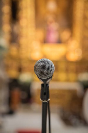 Mikrofon im Vordergrund, bereit, innerhalb einer Kirche oder eines religiösen Raumes verwendet zu werden. Verschwommener Hintergrund der Kirche.