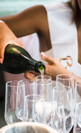 Bachelorette Party, Braut serviert Champagner über dem Tisch in hohen Champagnergläsern zu einer Gruppe von Brautjungfern. Vertikales Foto. Nahaufnahme