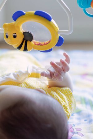 Liebendes Baby, das auf dem Rücken liegend mit einem Spielzeug interagiert. Konzentrieren Sie sich auf Ihre Hand. Körperliche und sensorische Entwicklung, Konzept. 