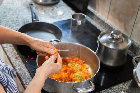 Detail einer Person, die auf der elektrischen Kochplatte mit Pfannen Essen kocht und das Essen schneidet, um den Eintopf zuzubereiten. Konzept Hausarbeit, Kochen zu Hause.