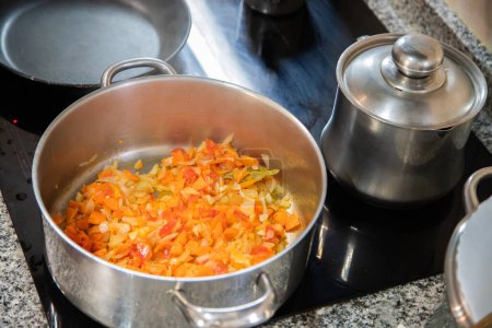 Detalle, cocina con vitrocerámica y sartén con ingredientes para preparar la comida. Concepto de tareas domésticas, cocinar en casa.