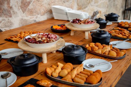Une table à buffet joliment aménagée présentant une variété d'entrées et de collations, y compris des plats de viande, des pâtisseries frites, prêts à déguster un délicieux repas.