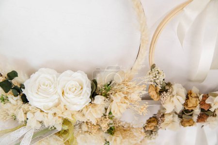 Wunderschön gefertigte Blumenkränze mit weißen Rosen und getrockneten Blumen, elegant auf weißem Hintergrund arrangiert, fangen die Essenz von rustikalem Charme und natürlicher Eleganz in der Wohnkultur ein.