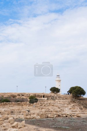 White lighthouse s under a partly cloudy sky surrounded by trees