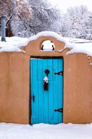 Téléchargez les photos : Scène hivernale de mur de pisé recouvert de neige avec une porte turquoise et ristra de piment rouge à Santa Fe, Nouveau-Mexique - en image libre de droit