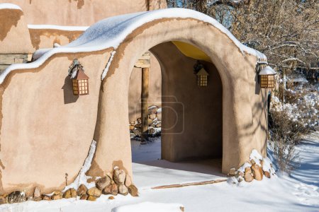 Snowy winter scene of a snow-covered adobe wall with an arched entrance in Santa Fe, New Mexico