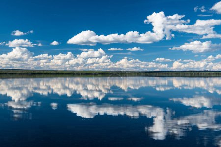 Téléchargez les photos : Scène paisible et idyllique de ciel bleu et de nuages blancs pelucheux reflétés dans les eaux d'un lac parfaitement calme - en image libre de droit