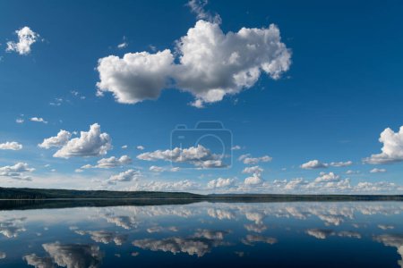 Téléchargez les photos : Scène tranquille et idyllique de ciel bleu et de nuages blancs moelleux reflétés dans les eaux d'un lac parfaitement calme - en image libre de droit