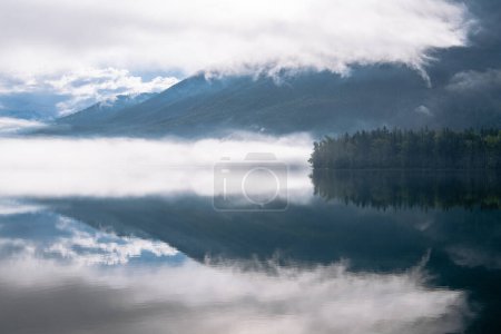 Téléchargez les photos : Scène paisible de montagnes brumeuses et de forêt reflétée dans un lac alpin au lac McDonald, parc national des Glaciers, Montana - en image libre de droit