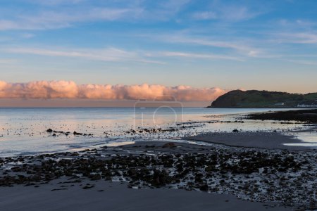 Téléchargez les photos : Une ligne de nuages colorés à l'horizon au coucher du soleil au-dessus de la plage et du littoral de la côte d'Antrim, Irlande du Nord - en image libre de droit