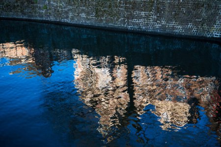 Téléchargez les photos : Bâtiments traditionnels néerlandais reflétés dans l'abstrait dans les eaux bleues ondulées d'un canal à Amsterdam, Pays-Bas - en image libre de droit
