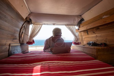 vista interior de una minivan con un joven rubio usando su portátil y trabajando cerca de la playa y el mar - viajero y nómada estilo de vida de la gente divirtiéndose 