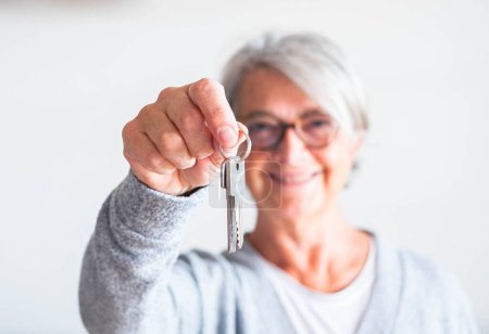 Téléchargez les photos : Une femme âgée et mature tenant la clé d'une maison ou d'une voiture - vendant sa propriété à quelqu'un prêt à louer ou à acheter - en image libre de droit