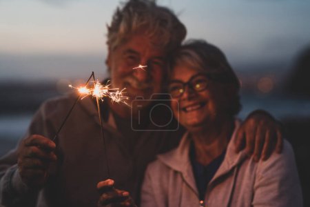 Photo for New year. close up of seniors celebrating the new year together at the beach with sparklers lights - Royalty Free Image