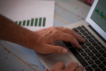 Téléchargez les photos : Gros plan des mains de l'homme sur un ordinateur portable travaillant dur pour créer une agence homme d'affaires avec des graphiques au bureau ou à la maison - en image libre de droit