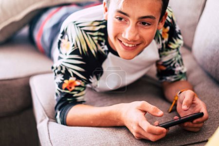 adolescent regardant des vidéos ou jouant à des jeux dans un téléphone intelligent en hiver couché sur un canapé dans le salon à la maison 