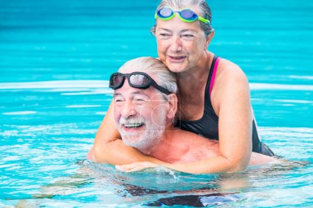 two pensioners or mature old people enjoying summer and vacations in the swimming pool together having fun smiling and laughing - couple of cute seniors in love - happy lifestyle and healthy concept 