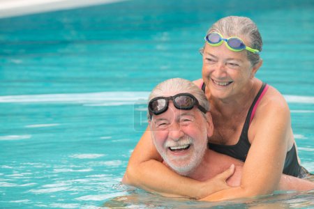 Téléchargez les photos : Couple de deux personnes âgées étreintes dans l'eau de la piscine - homme et femme actifs faisant de l'exercice ensemble à la piscine - étreintes d'amour - en image libre de droit