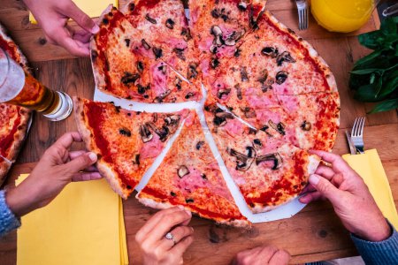 Foto de Primer plano de las manos tomando un trozo de pizza en una mesa de madera en casa al aire libre - grupo de personas celebrando algo o alguna fiesta - Imagen libre de derechos