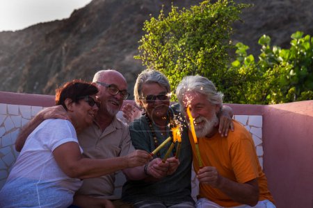 grupo de cuatro personas mayores juntas en el parque sentadas en el banco jugando con algo con fuego - personas maduras felices en año nuevo o celebrando algo o una fiesta 