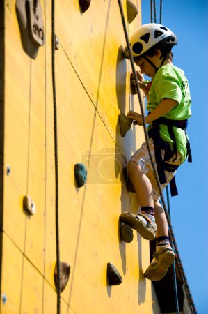 Foto de Niño escalador joven escalar una pared - niño divertirse solo mientras que subir - disfrutando del momento - cielo azul en el fondo - Imagen libre de derechos