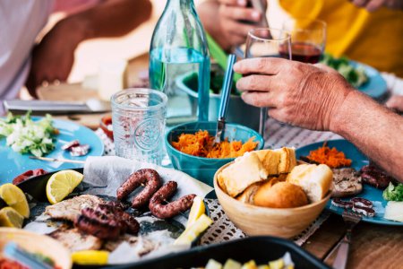 große Tafel mit Essen und Trinken - Senioren und Ältere halten ein Glas Wein zum Feiern - Familienfest zu Hause drinnen und draußen - kaukasische Menschen essen und kochen   