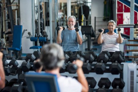Foto de Hombre maduro con su esposa haciendo ejercicio de bíceps en el gimnasio - fitness y el concepto de estilo de vida saludable - entrenar su cuerpo juntos - pareja de dos personas mayores - Imagen libre de derechos