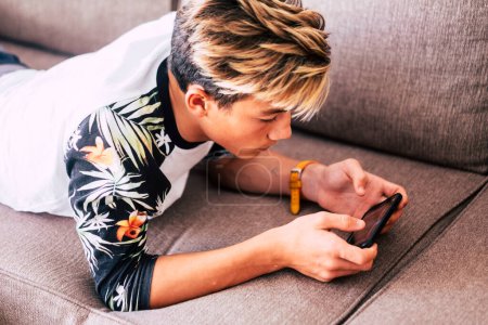 teenager watching videos or playing games in a smart phone  lying on a sofa in the living room at home