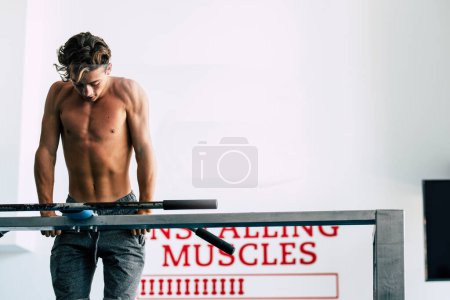 Téléchargez les photos : Adolescent faisant des musculations à la salle de gym - entraînement et travail de son corps - forme physique et homme en bonne santé - garçon actif avec de beaux muscles - en image libre de droit