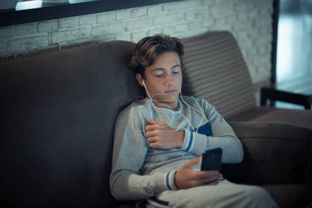 adolescent couché sur le canapé de la maison seul en utilisant son téléphone et écouter de la musique regarder des vidéos ou surfer sur le net la nuit les médias sociaux et le mode de vie accro aux réseaux et concept  