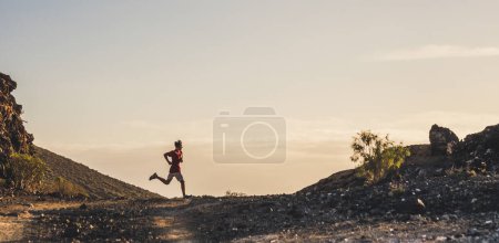 Téléchargez les photos : Un jeune homme qui court seul dans les montagnes et au sol pour être en bonne santé et actif - adolescent faisant de l'exercice et un mode de vie de trekking - en image libre de droit