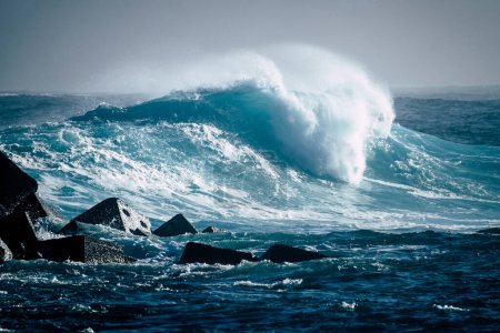 great and big wave breaking on her in a sea or ocean - ocean pacific or Atlantic blue sea with a rocks on the left 