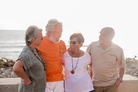 Foto de Grupo de personas mayores y personas maduras en la playa tomando juntos y divirtiéndose con el mar o el océano al fondo - cuatro personas - Imagen libre de derechos