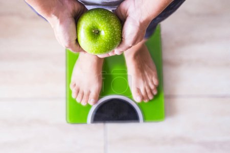 Photo for Woman or man on a weight scale showing an apple and select his lifestyle - good nutrition concept - Royalty Free Image