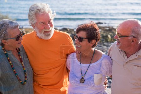 Gruppe von Senioren und erwachsenen Menschen am Strand zusammen und Spaß mit dem Meer oder dem Meer im Hintergrund - vier Personen