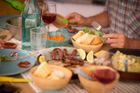 Foto de Hermoso momento de estilo de vida familiar en casa, comer y beber en casa sobre la mesa - hombre con gafas de sol tomando una verdura - mesa llena de comida y ensalada al aire libre - Imagen libre de derechos