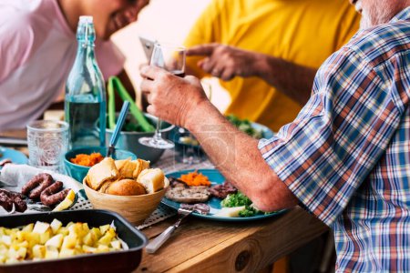 Photo for Big table full of food life bread, meat, vegetables - some people sitting next to the table eating and drinking vine and water - celebration - a lot of salad and all of types of food - Royalty Free Image