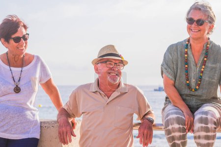 drei Senioren und erwachsene Menschen am Strand mit dem Meer im Hintergrund, die zusammen Spaß haben und lachen  
