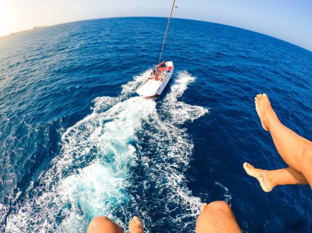 Nahaufnahme und Porträt der Beine zweier Menschen, die in der Luft fliegen, während ein Boot sie zieht - Erwachsene, die im Sommer zusammen Spaß beim Parasklettern haben und ihren Urlaub genießen 
