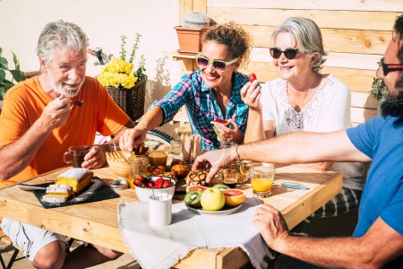 Gruppe glücklicher Menschen frühstückt zu Hause auf der Terrasse zusammen mit der Liebe - Tochter, Sohn, Oma und Opa essen und trinken - ein paar Senioren verheiratet und Erwachsene 