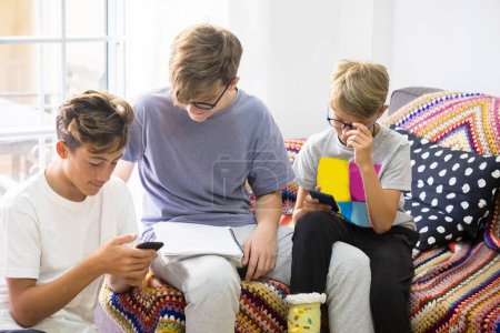 Gruppe von drei Teenagern, die auf dem Sofa sitzen und auf die Telefone schauen und ihnen die Hausaufgaben ansehen, ob das stimmt 
