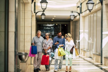 Photo for Group of people go shopping together with a lot of bags on their arms and holding with hands at mall or big store - family enjoying buying clothes together of doing gifts for Christmas - Royalty Free Image
