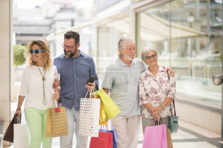 Photo for Two couples of two adults and two seniors go shopping together at the mall with a lot of bags with clothes and more on their hands - four people happy enjoying - Royalty Free Image