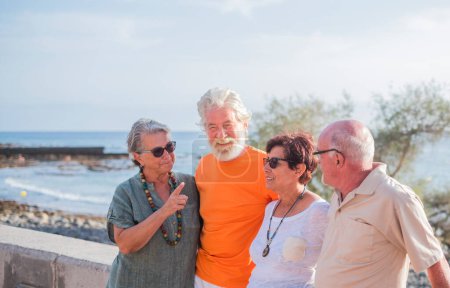 grupo de personas mayores y personas maduras en la playa tomando juntos y divirtiéndose con el mar o el océano al fondo - cuatro personas