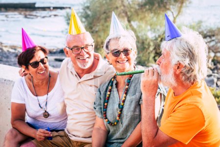 groupe de personnes âgées et matures assis à la plage avec la casquette de la fête et à la recherche d'un homme et rire - fête ou concept d'anniversaire 